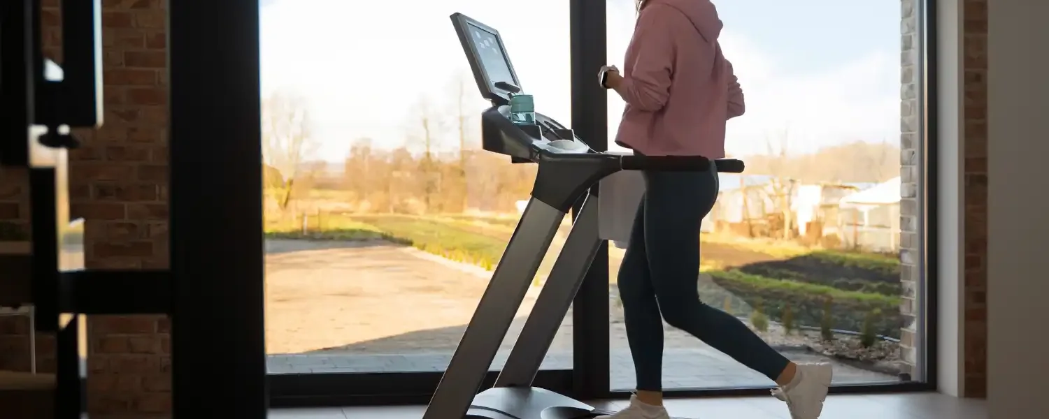 Pessoa utilizando uma esteira residencial em um espaço fitness funcional com vista para o exterior, ideal para montar um espaço fitness em casa.