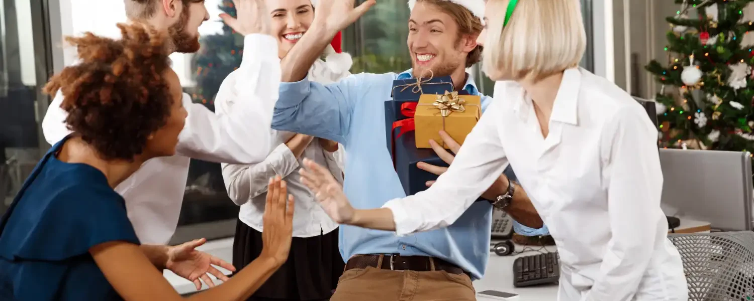 Equipe de colegas de trabalho celebrando ações sociais corporativas no fim de ano, com decorações natalinas e um presente, promovendo impacto social real.