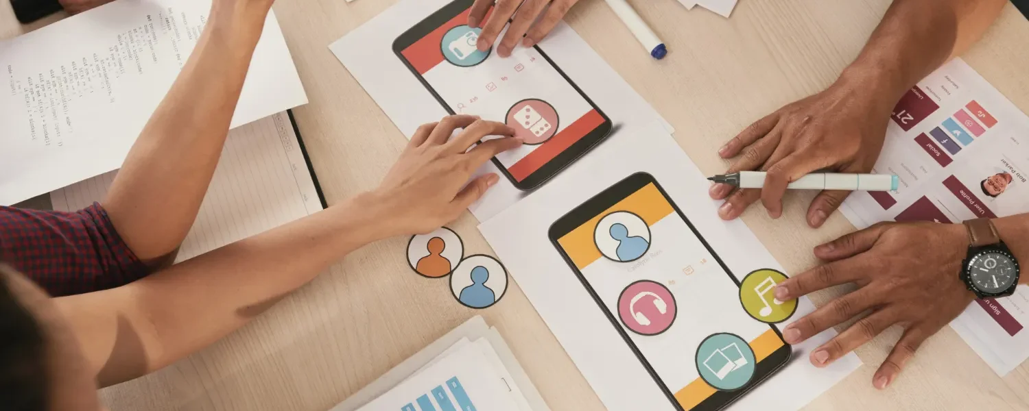 Comunicação Integrada: Como Alinhar Todos os Canais de uma Marca: Equipe reunida em mesa com gráficos, planilhas e aplicativos em celulares, enquanto pessoas apontam e discutem ideias para alinhar canais de uma marca e integrar comunicação. Treinamento e planejamento colaborativo.