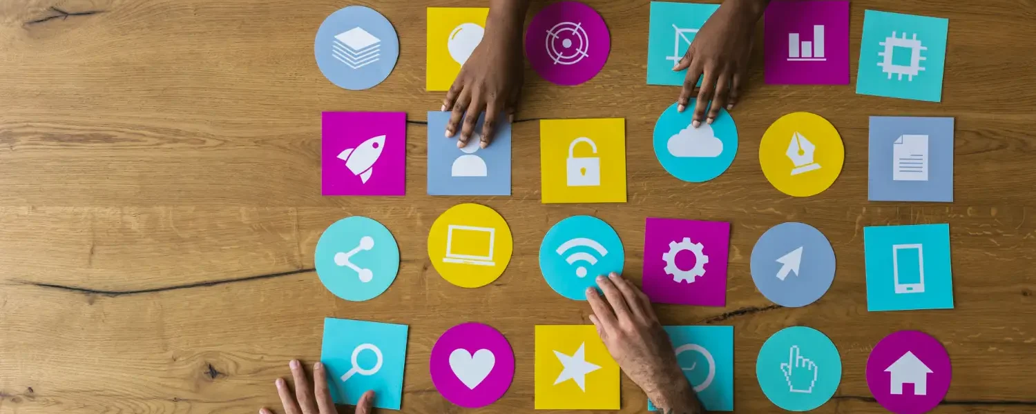 Mãos organizando ícones coloridos de redes sociais e tecnologia sobre uma mesa de madeira, representando engajamento, comunicação e Marketing de comunidade: Como marcas podem criar relacionamentos mais próximos com seus consumidores.
