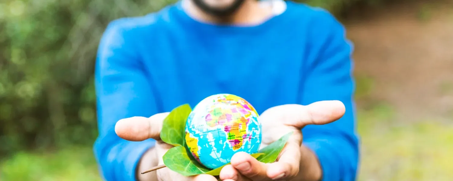 Homem em ambiente externo segura um pequeno globo de papel com folhas verdes ao redor, simbolizando Sustentabilidade no cotidiano: Pequenas mudanças que ajudam a reduzir o desperdício